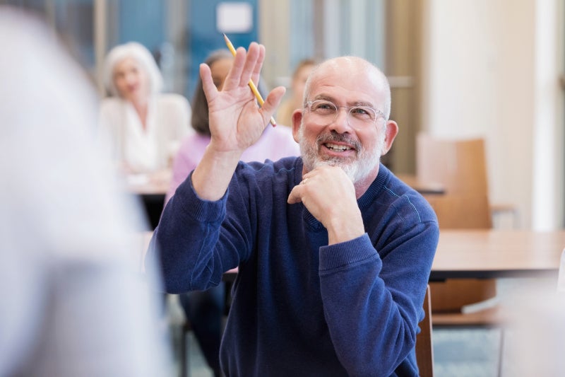 Senior man raising his hand to ask a question at an educational event